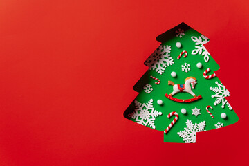 Christmas tree cutout with festive toy horse, candy canes, and snowflakes on a red background.