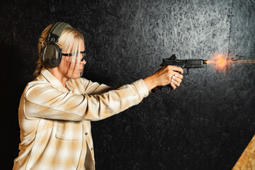 A focused woman wearing safety glasses and ear protection fires a modern handgun with an optic sight at a shooting range.