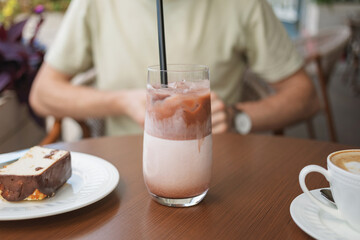 Close-up of a man sitting at table on summer terrace and enjoying a refreshing iced cacao drink with delicious cake.