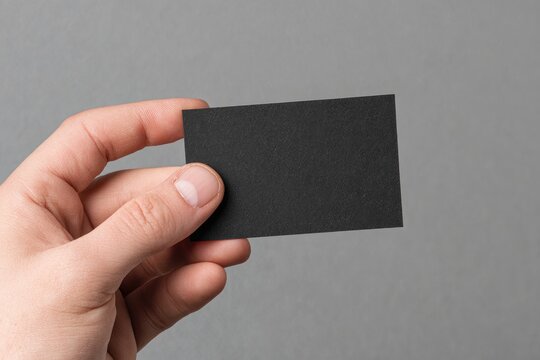 A hand holds a blank black business card against a gray background (2)