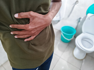 Man holding stomach in pain near toilet bathroom scene illustrating digestive issues diarrhea...