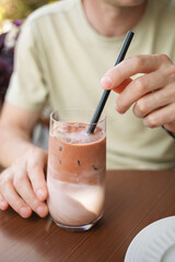 Close-up of a man sitting at table on summer terrace and enjoying refreshing iced latte coffee. 