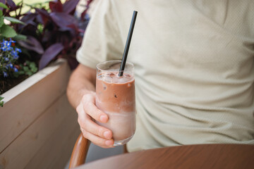 Close-up of a man sitting outdoors in summer with a glass of iced mocha coffee.