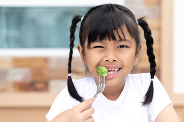 Happy child holding a fork with broccoli ready to eat, concept of healthy food, vegetarian diet, nutrition for kids, wellness lifestyle, healthy eating habits, and organic vegetables for children.