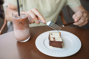 Close-up of a man enjoying a slice of cheesecake and a glass of iced latte coffee, while sitting on the terrace of a cafe.