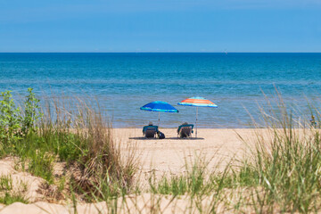 couple beach chairs on sandy beach under colorful umbrellas looking out at blue and turquoise water...