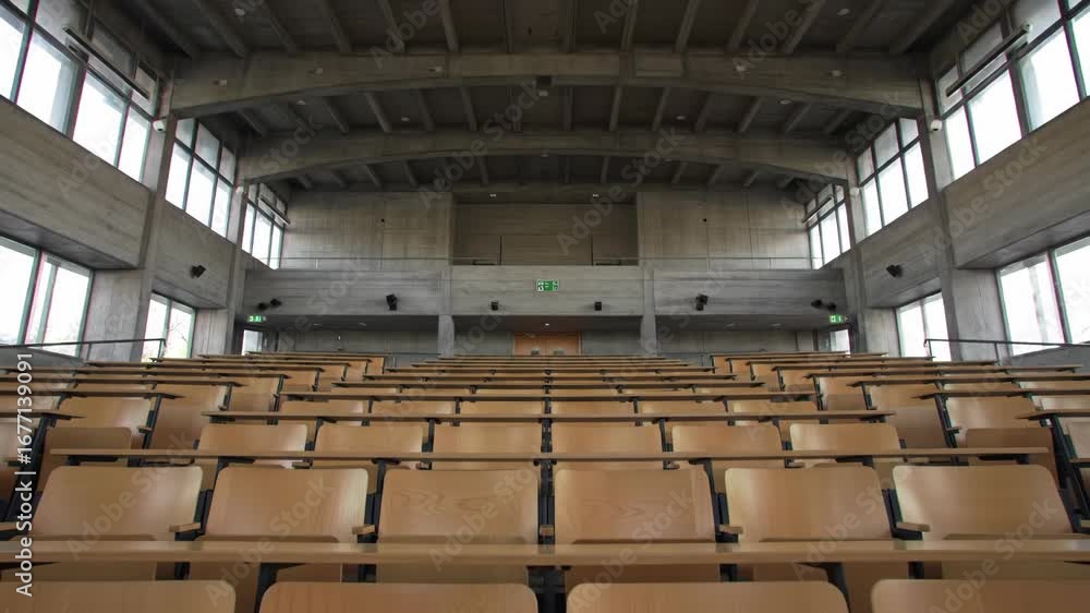 Poster empty lecture hall featuring rows of wooden seats in a concrete building with large windows, suitabl