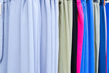 A row of brightly colored pants hangs on a clothing rack, showing a variety of colors and textures