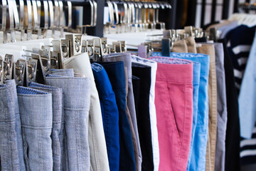 A row of brightly colored pants hangs on a clothing rack, showing a variety of colors and textures