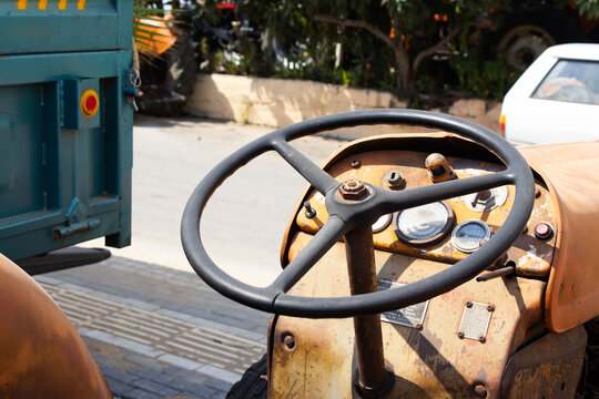 A close-up shot of a rusty, old tractor's steering wheel and dashboard, conveying a sense of hard work and age