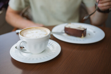 Close-up of a man enjoying a slice of delicious cheesecake and a cup of coffee, sitting on the terrace of a cafe.