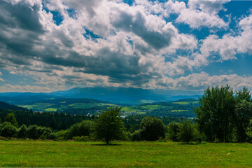 Sweeping view over fields, forests, and a village toward the Tatra Mountains beneath layered...