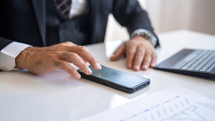 Businessman doing calculations with smart mobile phone at office desk.
