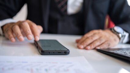 Businessman doing calculations with smart mobile phone at office desk.