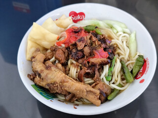 A complete bowl of chicken noodles with claws, dumplings, chicken pieces and red chili sauce on top, traditional Indonesian food.