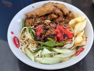 A complete bowl of chicken noodles with claws, dumplings, chicken pieces and red chili sauce on top, traditional Indonesian food.