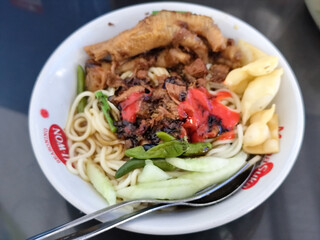 A complete bowl of chicken noodles with claws, dumplings, chicken pieces and red chili sauce on top, traditional Indonesian food.