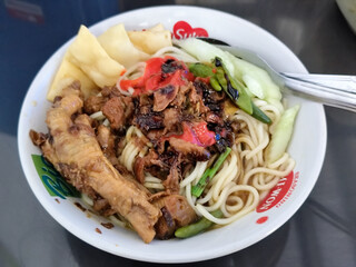 A complete bowl of chicken noodles with claws, dumplings, chicken pieces and red chili sauce on top, traditional Indonesian food.