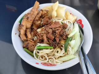A complete bowl of chicken noodles with claws, dumplings, chicken pieces and red chili sauce on top, traditional Indonesian food.