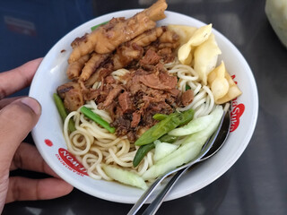 A complete bowl of chicken noodles with claws, dumplings, chicken pieces and red chili sauce on top, traditional Indonesian food.