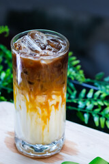 Close-up of iced caramel macchiato in a tall glass, layered with milk, caramel drizzle, and espresso over ice cubes.