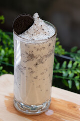 Glass of Oreo milkshake with whipped cream texture, topped with a chocolate cookie, served in a tall glass on wooden table.