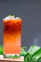 Refreshing iced Thai tea with gradient orange and pink layers, served in a tall glass with ice cubes and mint leaves.