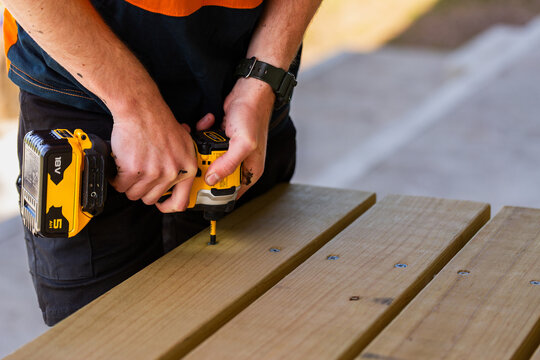 Apprentice worker using drill to make picnic table