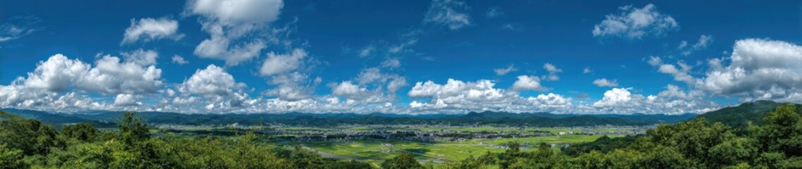 Obraz premium Panoramic view of a valley with lush green landscape, puffy white clouds, and a vibrant blue sky