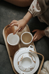 Child Reaching for Cups on Wooden Tray