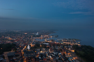 Aerial skyline cityscape of Thisted, Denmark at night, showing the glowing harbor, white church, city lights, and scenic coastline on the Limfjord