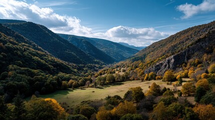 A vast valley nestled between steep, forested mountains displays a panorama of autumn colors.