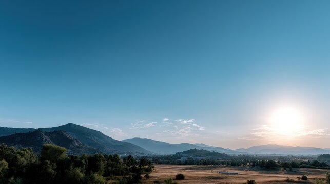 A vast landscape unfolds, showcasing a serene vista of rolling hills, lush green trees, and a clear, vibrant blue sky, illuminated by a golden sunrise. - Powered by Adobe