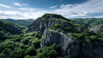 A verdant valley nestled amongst dramatic, dark gray cliffs under a bright sky filled with fluffy clouds.