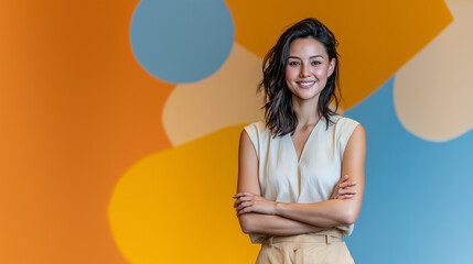 Fototapeta premium Smiling young woman standing confidently with crossed arms in front of colorful geometric orange and blue background, modern business portrait with creative and professional vibe
