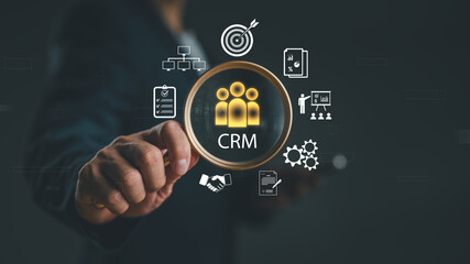 Businessman holding magnifying glass over CRM icon surrounded by marketing, analytics and customer management symbols. Concept of customer relationship management and business strategy.