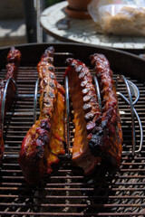 Four racks of ribs are cooked on a metal rack inside a charcoal grill in an outdoor setting.