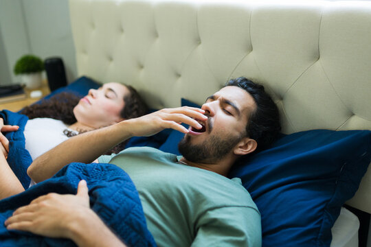 Hispanic man yawning while waking up next to partner in bed