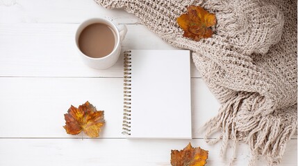White blank notebook mockup on white wooden table with autumn leaves, coffee cup and knitted blanket, flat lay top view with copy space for blog design, social media content