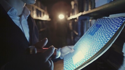 A young man with a flashlight at night looking documents in libraries