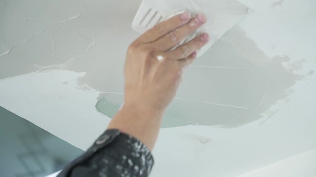 Worker using a putty knife to apply and smooth plaster on a ceiling surface
