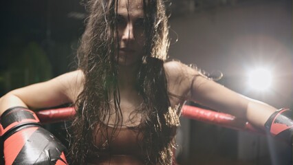 Sport boxing girl wearing black boxing gloves sitting in corner .