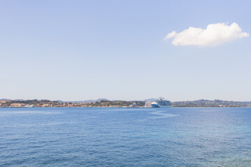 White cruise ship anchored in calm Mediterranean waters near coastal town with mountains, hills,...