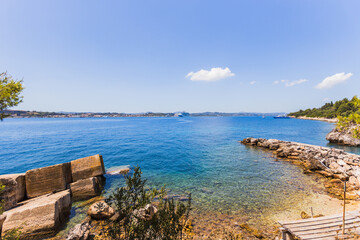 Beautiful Greek shoreline with a small pier, turquoise sea, luxury yacht, and distant cruise ship...