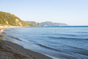 Serene Mediterranean sandy beach with clear turquoise water, rolling waves, yellow buoys, and...