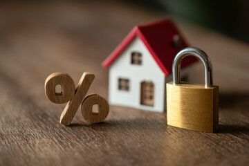 Home security and interest rates: A golden lock protects a miniature house next to a percentage sign.
