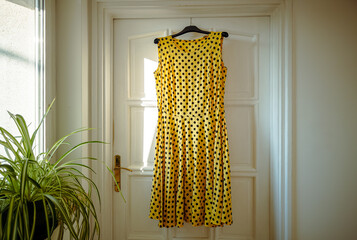 Yellow polka dot dress hangs on a hanger on the door