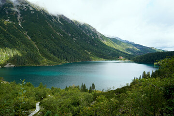 Emerald mountain lake surrounded by lush forested slopes and towering peaks, reflecting light and creating serene natural landscape.