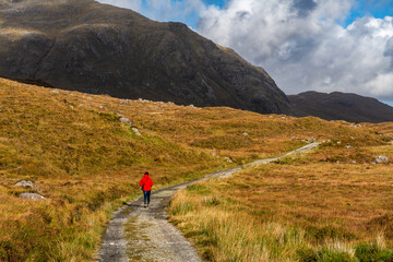One figure in a red jacket walks along a narrow path through golden moorland, leading towards...