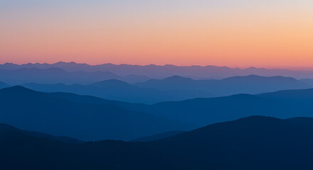 Fototapeta premium Layered mountain silhouettes at dusk create a gradient of tranquil blues merging with the warm hues of the twilight